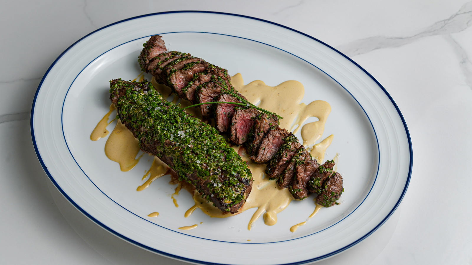 Chive Crusted Hanger Steak on sauce and white plate