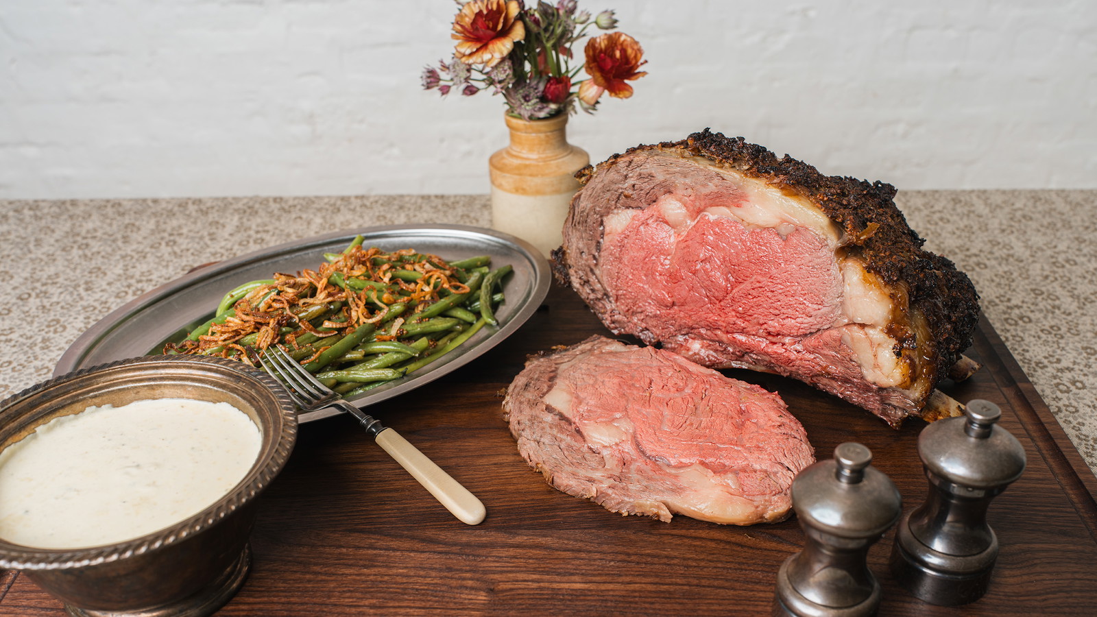 Wagyu Bone-In Prime Rib on a table with green bean side and flower vase