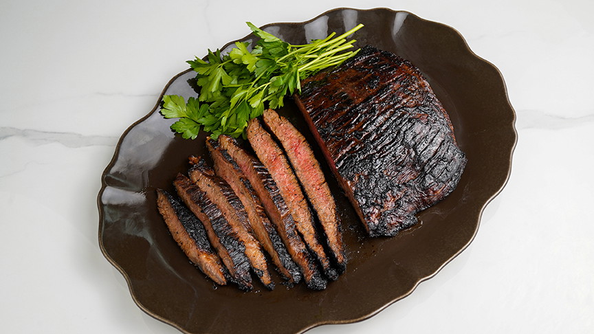marinated and cooked flank steak on a black plate 