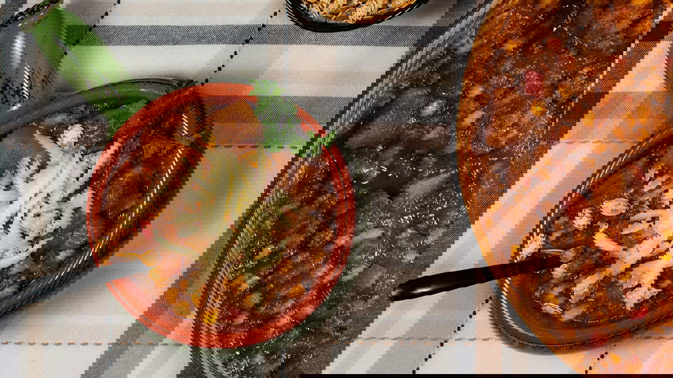 Top down image of a bowl of stew, made with juicy Halal ground lamb and chunks of pumpkin, onion, red pepper, corn, and beans. Seasoned and simmered and topped with Monterey Jack cheese and pumpkin seeds.