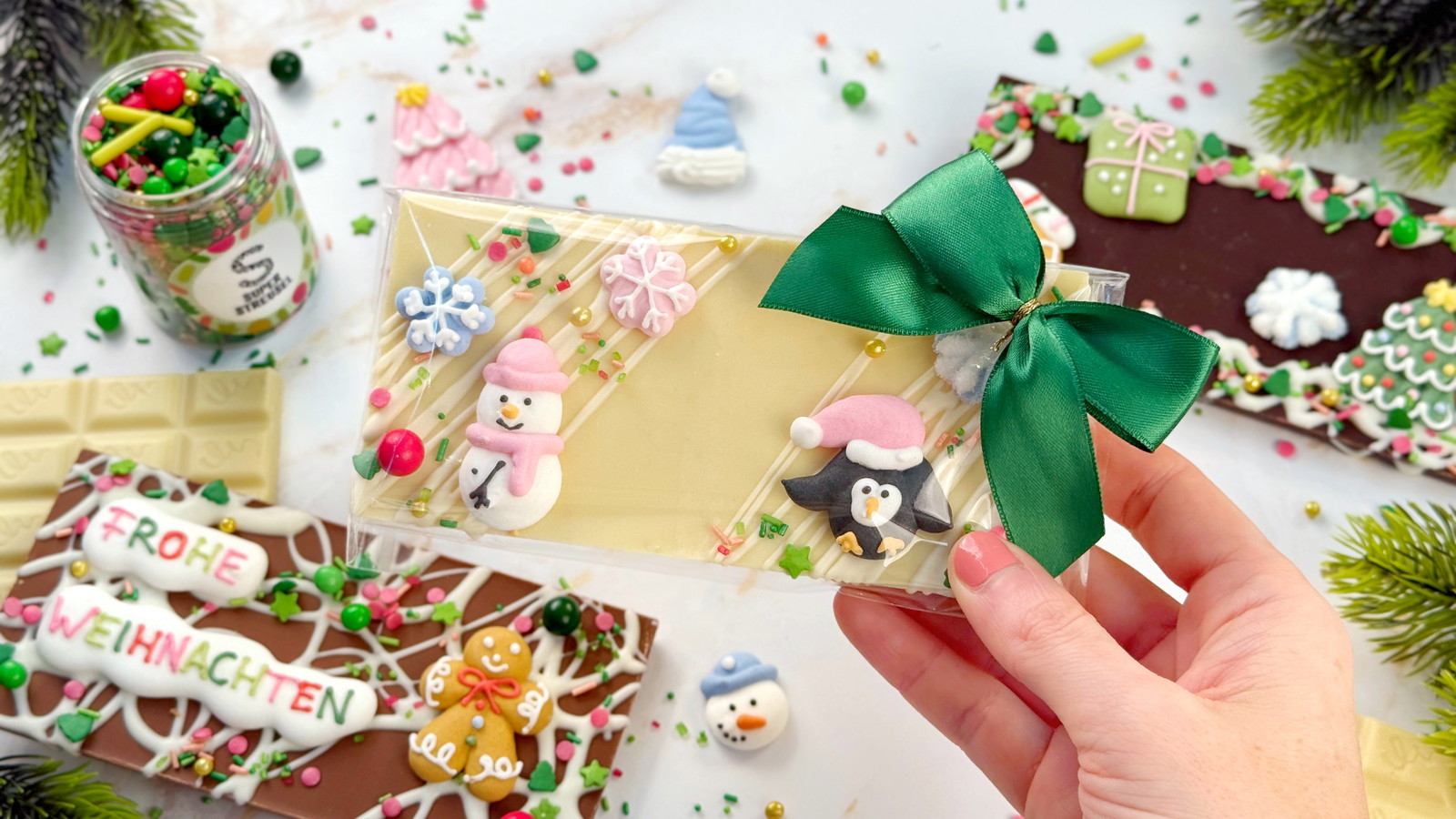 Weihnachts-Schokoladentafeln aus weißer, Vollmilch- und Zartbitterschokolade, dekoriert mit weißem SuperDrip, StreuselMix WichtelWald sowie SuperDinger EsSchneitEsSchneit und FroheWeihnacht. Festliche Schokolade als Geschenkidee.