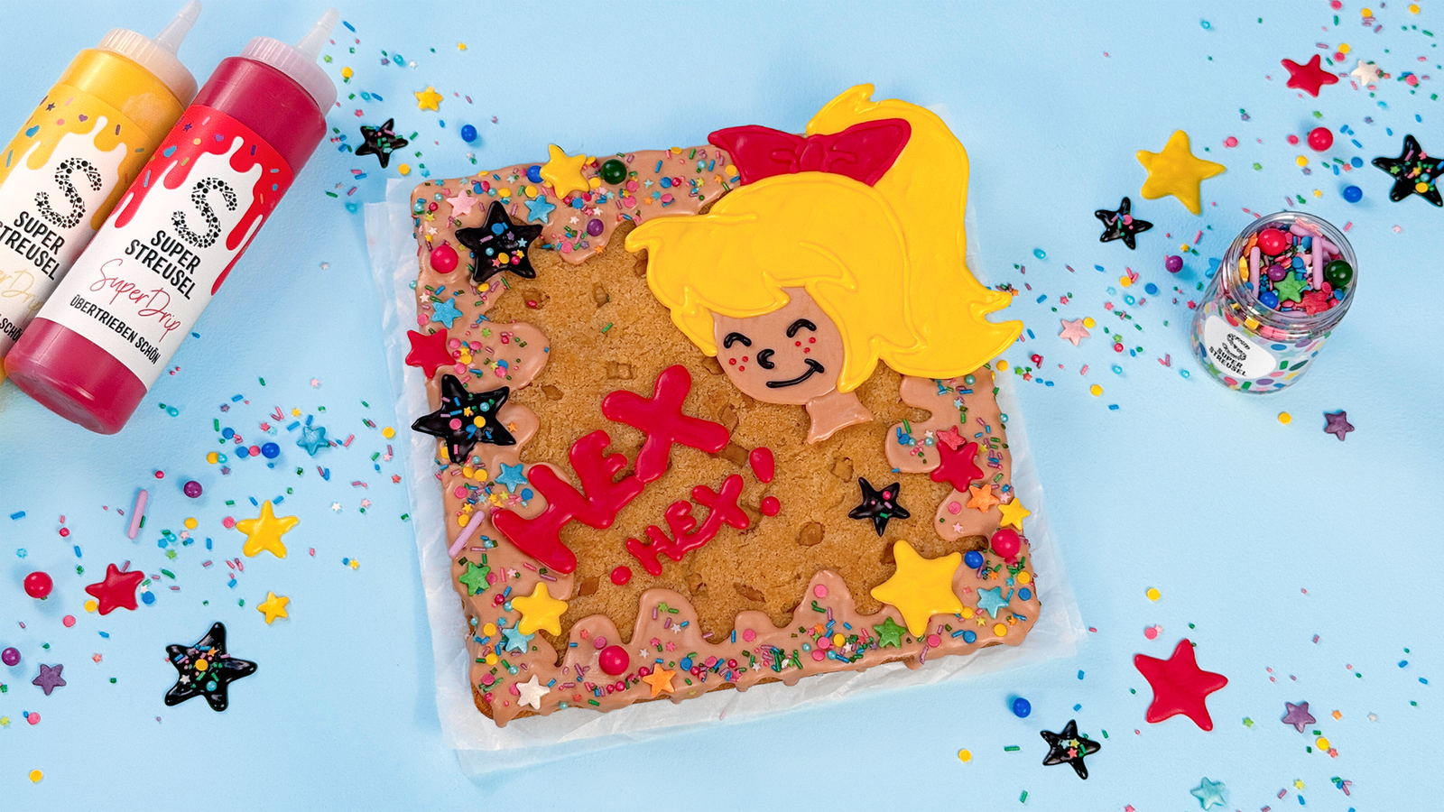 Bibi-Blocksberg-Blondie mit gelbem, rotem, schwarzem und Salted-Caramel-SuperDrip dekoriert, mit Hex-Hex-Schriftzug und Sternen aus SuperDrip, verziert mit StreuselMix SternenRegen. Magischer Kuchen im Hexenstil.