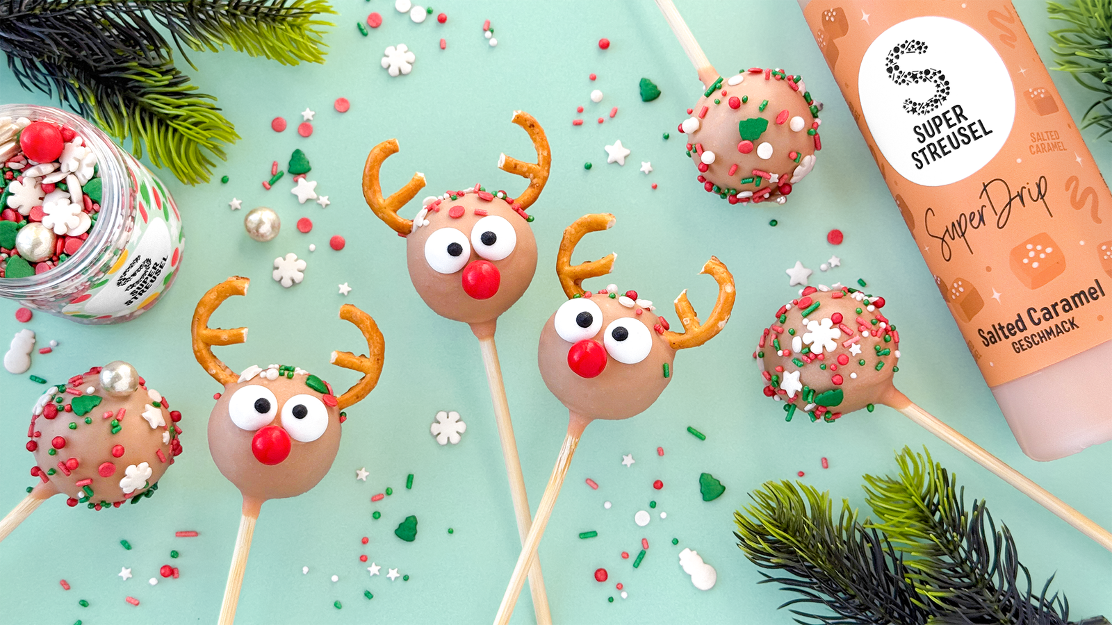 Rudolf Caramel Brownie CakePops: Brownie-Kugeln am Stiel, mit Salted-Caramel-SuperDrip überzogen, dekoriert mit Salzbrezel-Geweihen, KullerAugen und roter Nase aus StreuselMix KlingGlöckchen; daneben bunte Streusel-CakePops.