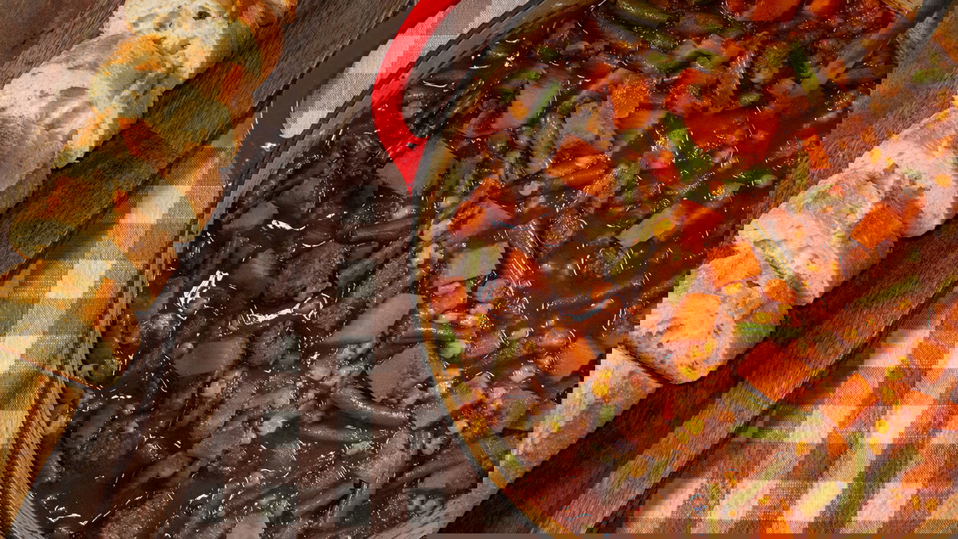 Top down image of a large pot of hearty beef stew. Made with chunks of sweet potato, onion, sliced green beans, and corn with chunks of tender Halal beef. Served with bread.