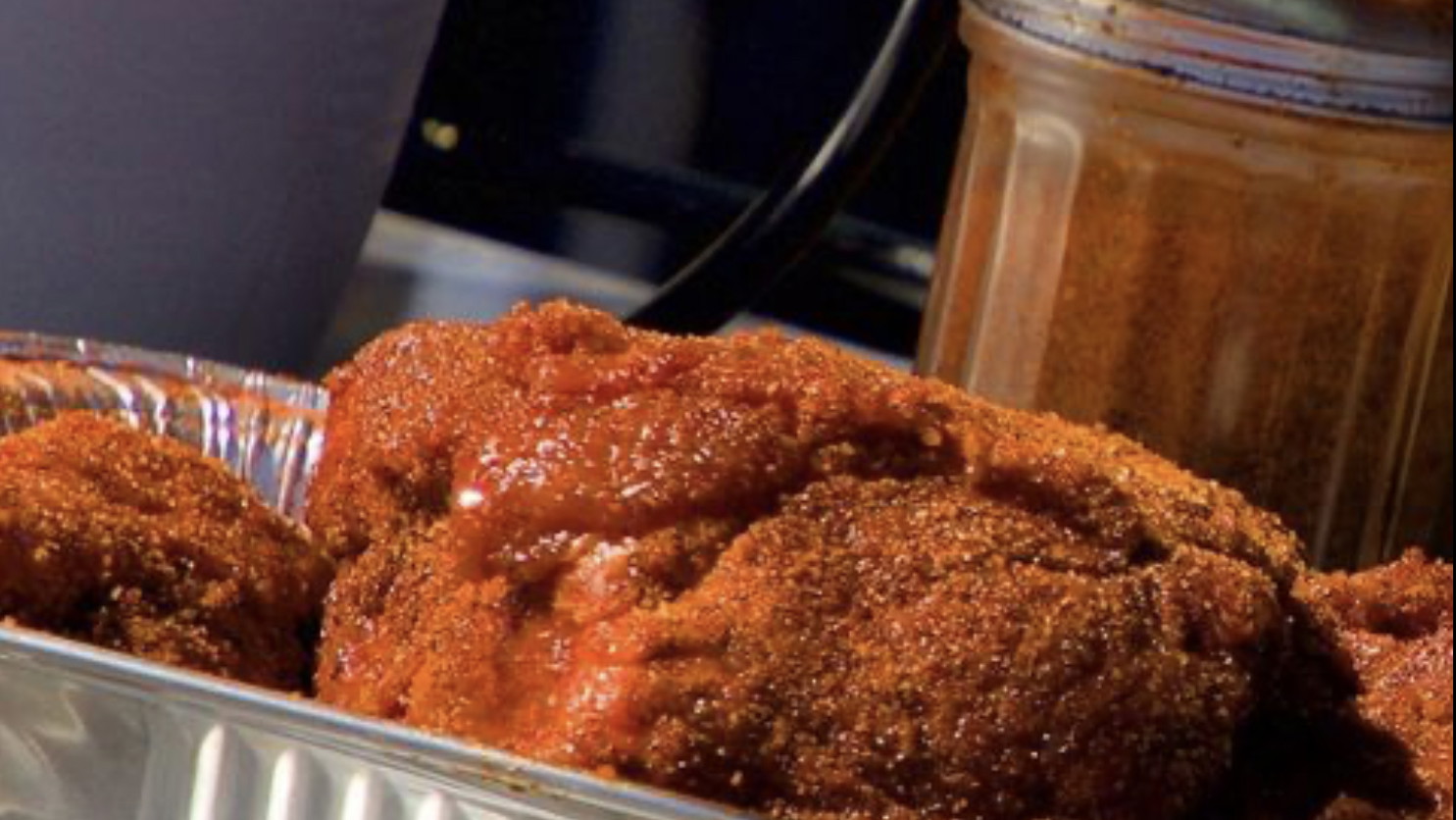 Raw Boston Butt seasoned in Foil tray and Rub Shaker in background