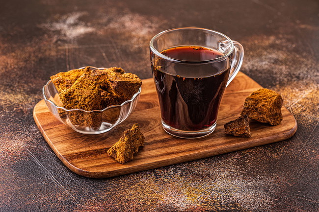 Chaga Tee in einem Glas mit einem Brocken Chaga Pilz daneben