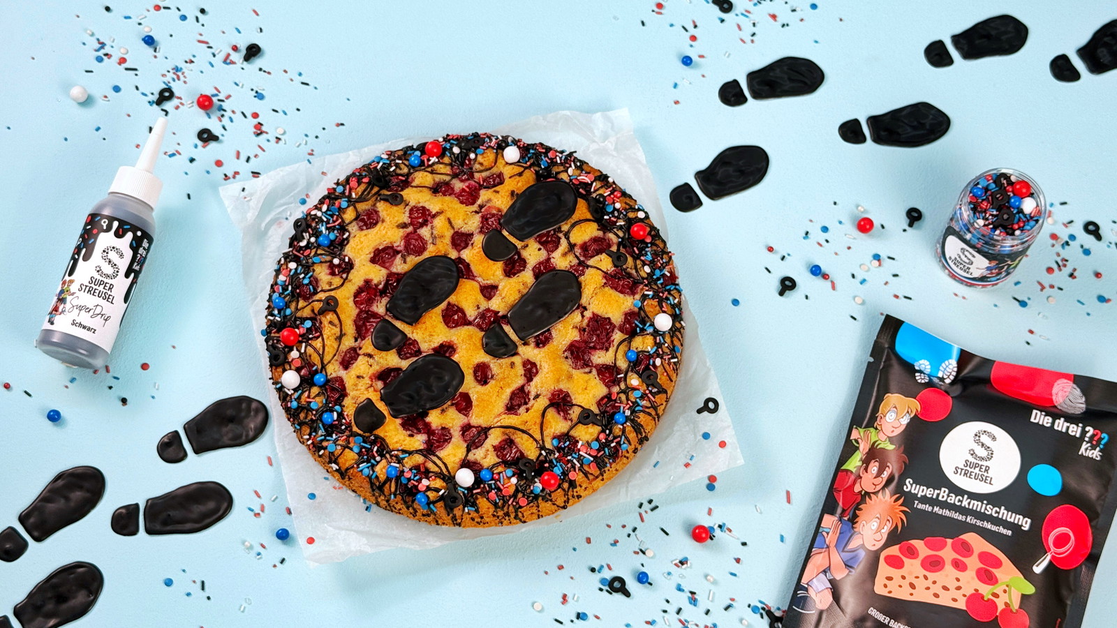 Kirschkuchen nach Tante Mathildas Rezept, dekoriert mit schwarzen SuperDrip-Fußspuren und StreuselMix DieDrei???Kids. Detektivischer Kinderkuchen mit Spuren-Deko aus SuperDrip.