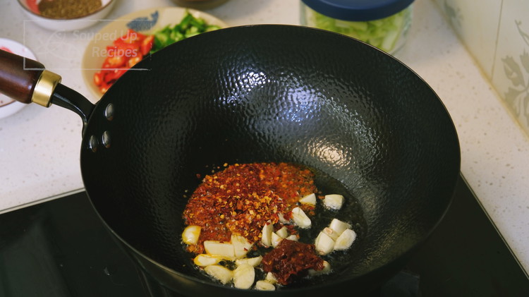 Image of Add about 2 tbsp of oil, diced garlic, 1-2 Tbsp of red pepper flakes, and 1 tbsp of Sichuan Dou Ban Jiang to the wok. Stir over low heat for a minute or 2.