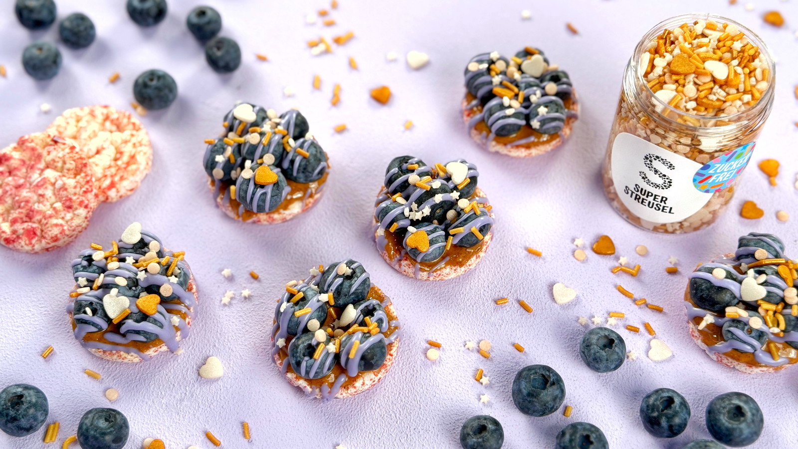 Mini-rijstwafels met amandelpasta en verse blauwe bessen, afgewerkt met lavendelkleurige SuperDrip en suikervrije StreuselMix FallingInLove. Snelle snack zonder bakken.
