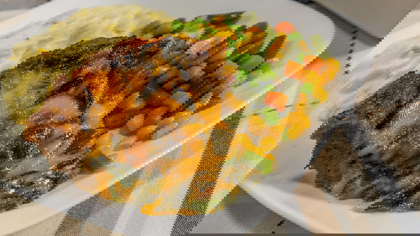 A slice of halal meatloaf with melty cheese and spinach, served with mashed potatoes and mixed vegetables.