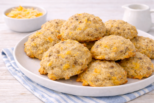A plate of golden, cheesy sausage drop biscuits piled high on a white plate, showcasing their crispy edges and melty cheese.