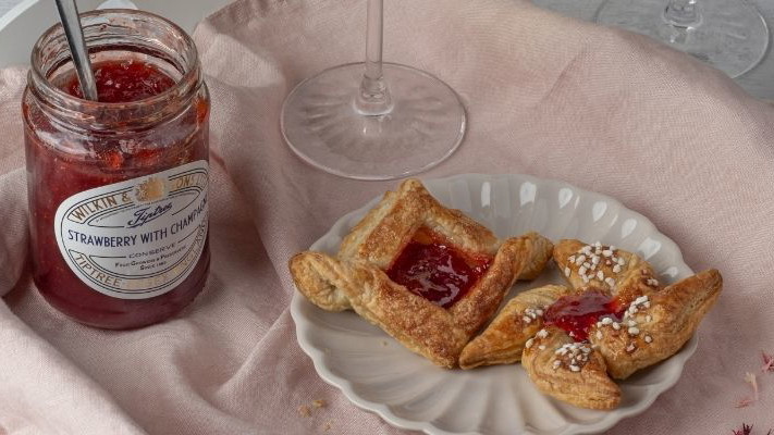 A jar of Tiptree Strawberry with Champagne Conserve next to a freshly baked mini pastry