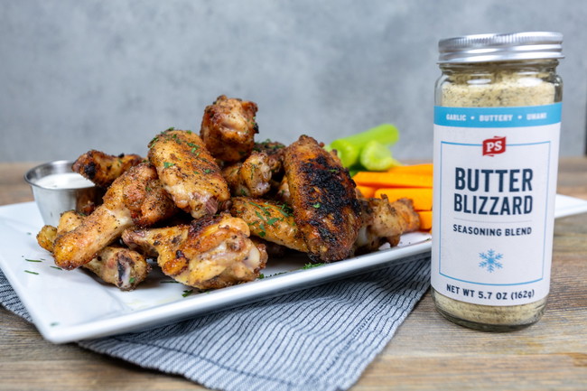 Butter Blizzard Grilled Chicken Wings Grilled chicken wings stacked on a white plate, seasoned with PS Seasoning Butter Blizzard and garnished with herbs. Served with carrot and celery sticks, ranch dressing, and a jar of Butter Blizzard seasoning on the side. Butter Blizzard grilled chicken wings, PS Seasoning wing recipe, garlic butter wings, grilled wings with crispy skin, BBQ chicken wing recipe, two-zone grilled wings, butter basted chicken wings