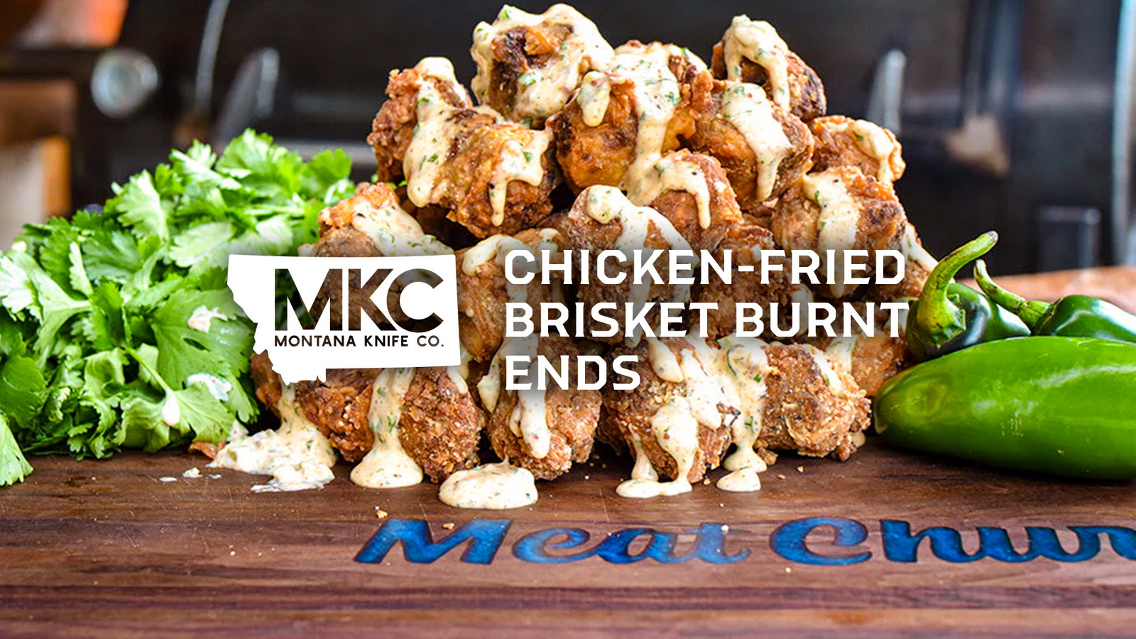 Close-up of chicken‑fried brisket burnt ends drizzled with creamy sauce, with peppers and herbs arranged beside them.