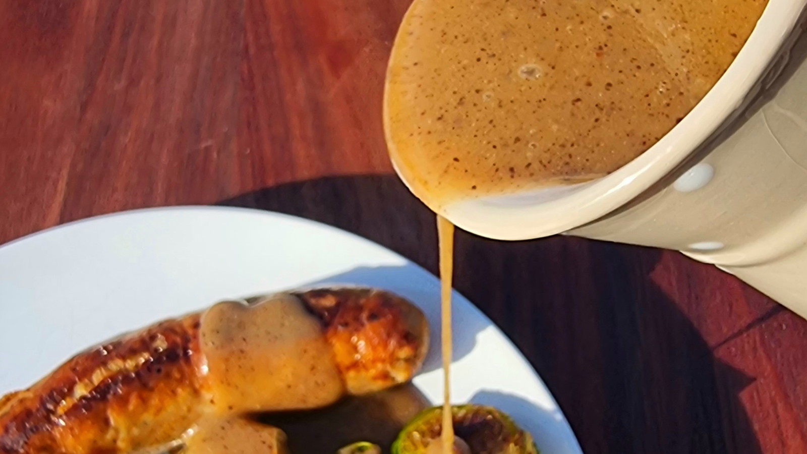 Black Garlic Gravy being poured over sausages on a plate
