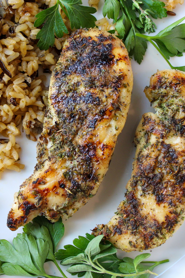 Grilled garlic and herb chicken tenderloins served with brown and wild rice, garnished with fresh herbs and sliced radishes on a white plate.