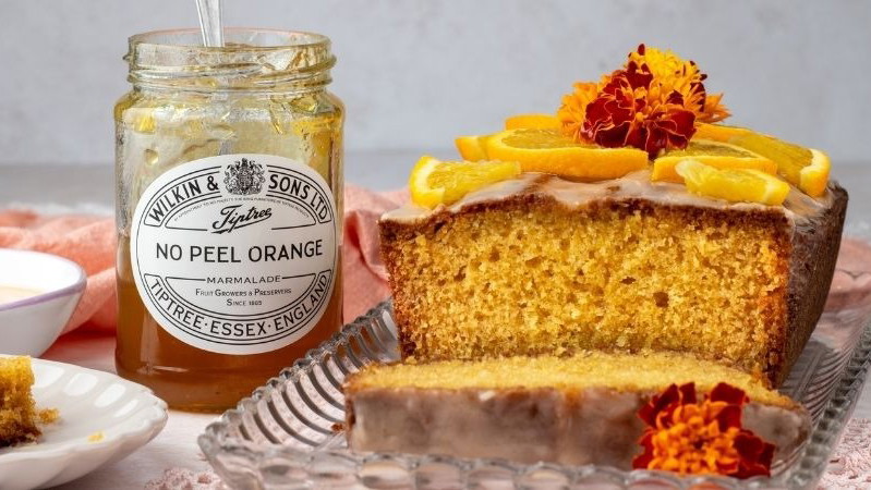 An orange loaf cake next to a jar of Tiptree No Peel Orange Marmalade