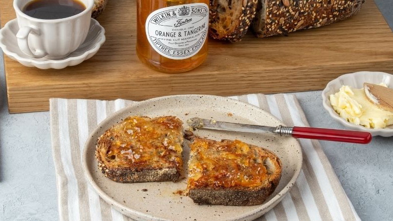Tiptree Orange and Tangerine Marmalade on Toast, next to an open jar and a cup of tea.