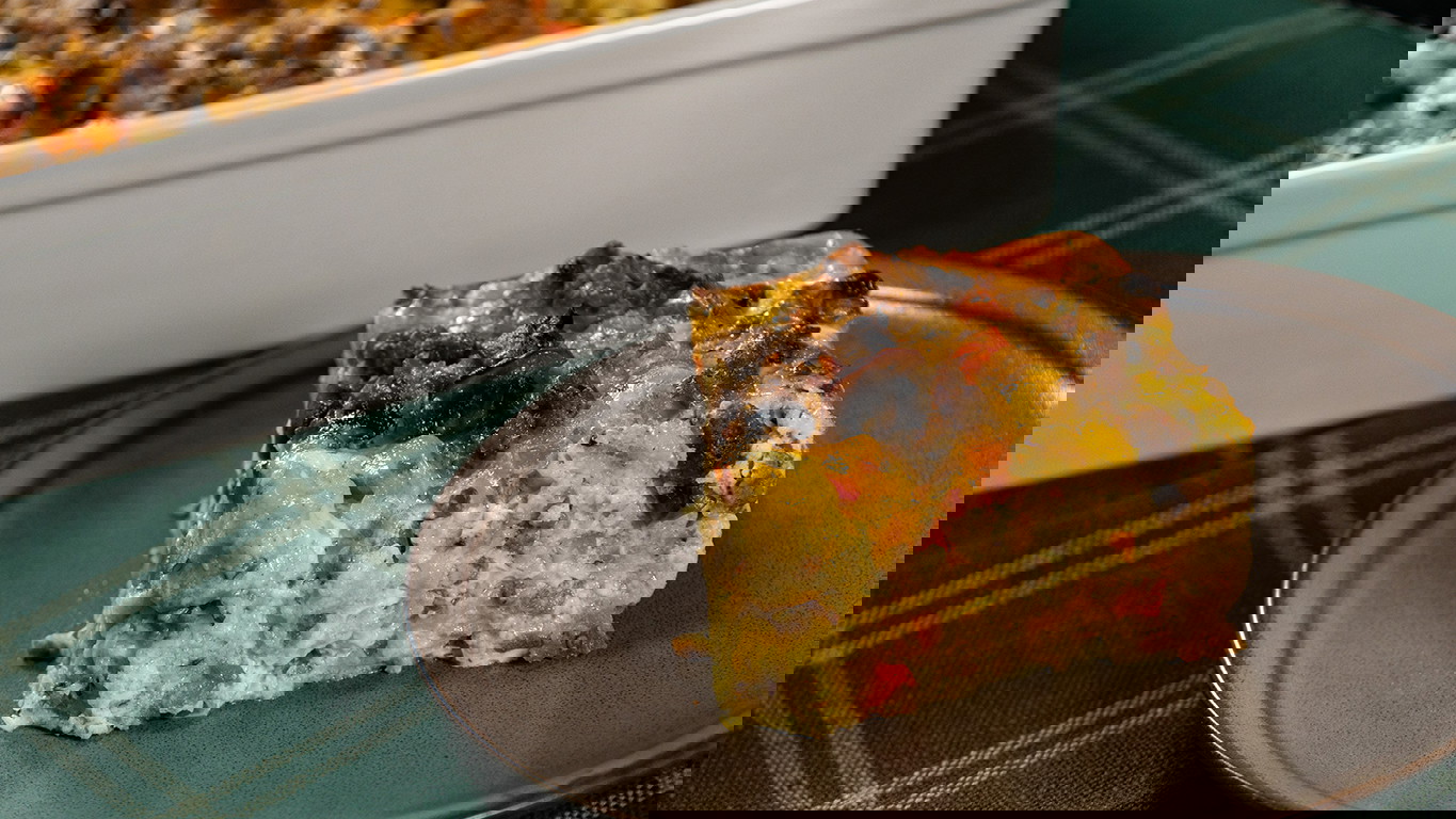 I slice of breakfast casserole of egg, cheese, and diced onion, mushroom, and tomato with a crumble of savory Halal breakfast sausage mixed throughout..