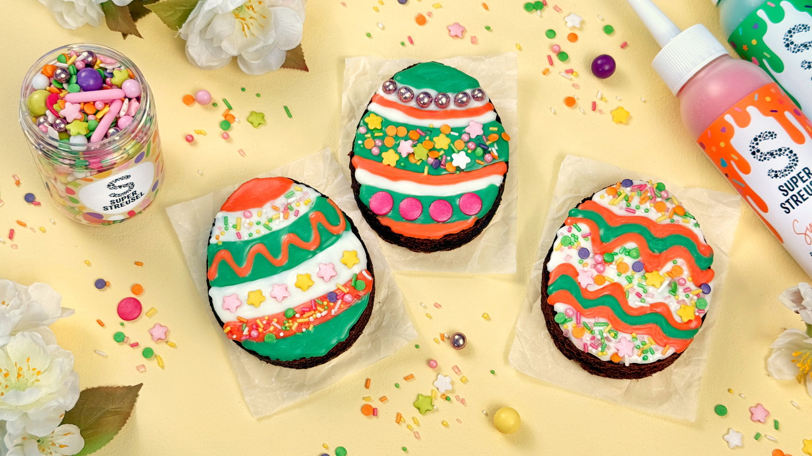 OsterEi Brownies aus ausgestochenem Brownie mit SuperDrip Grün, Orange und Weiß sowie StreuselMix FrühlingsFieber dekoriert.
