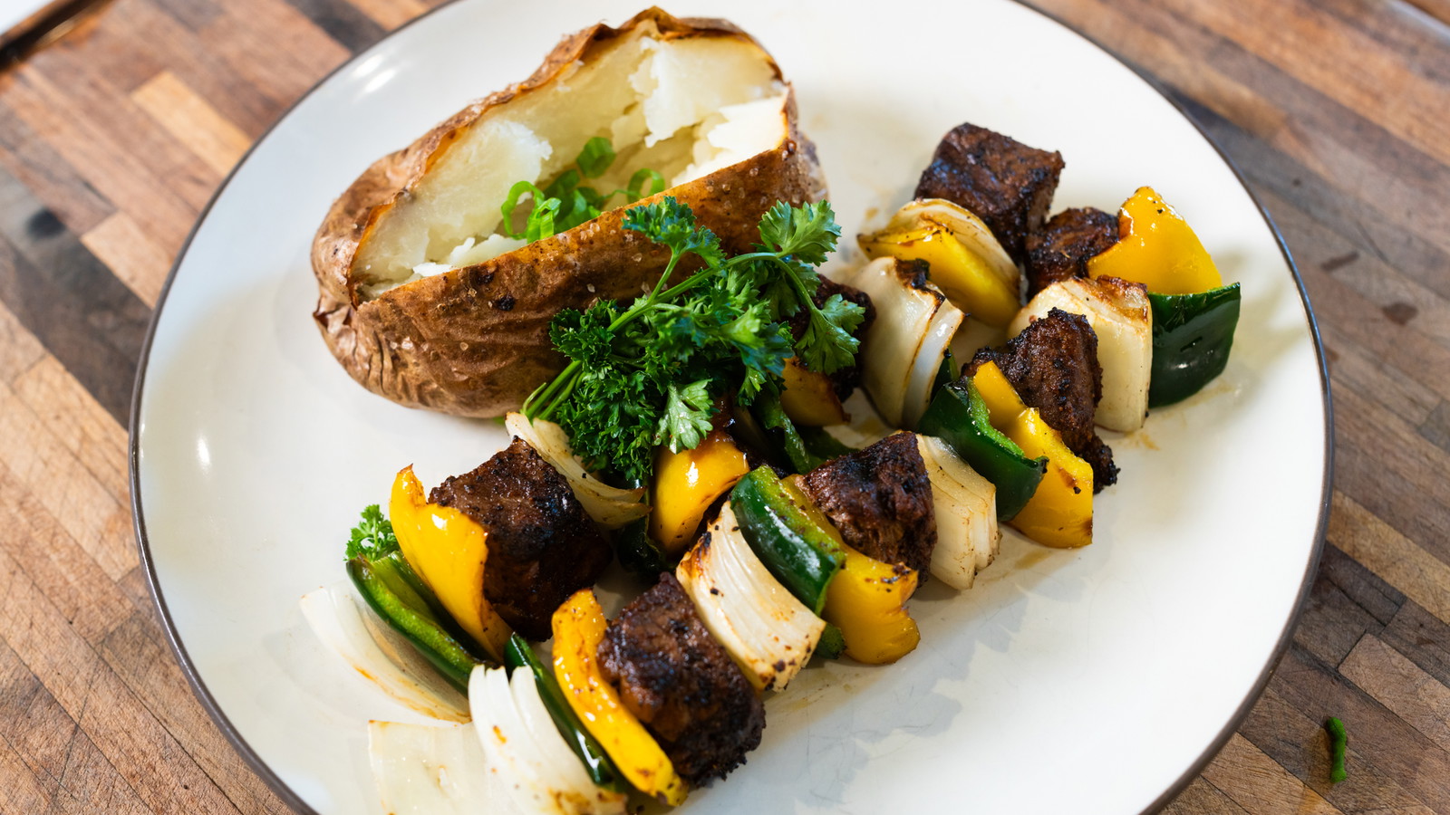 Steak Kebabs, arrangged on a plate with a baked potato.