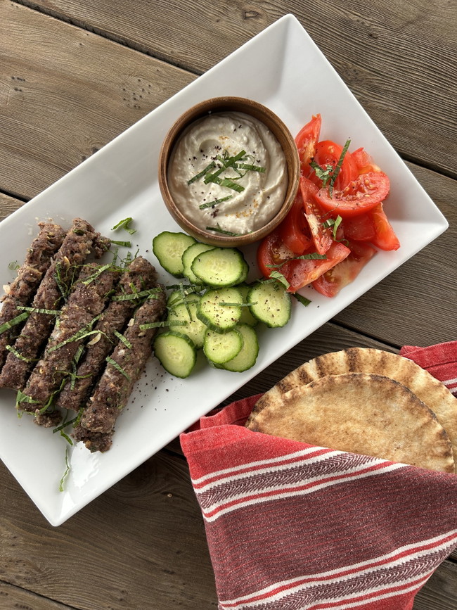 Beef kofta on a plate with cucumber, tomato, tahini yogurt, and pita