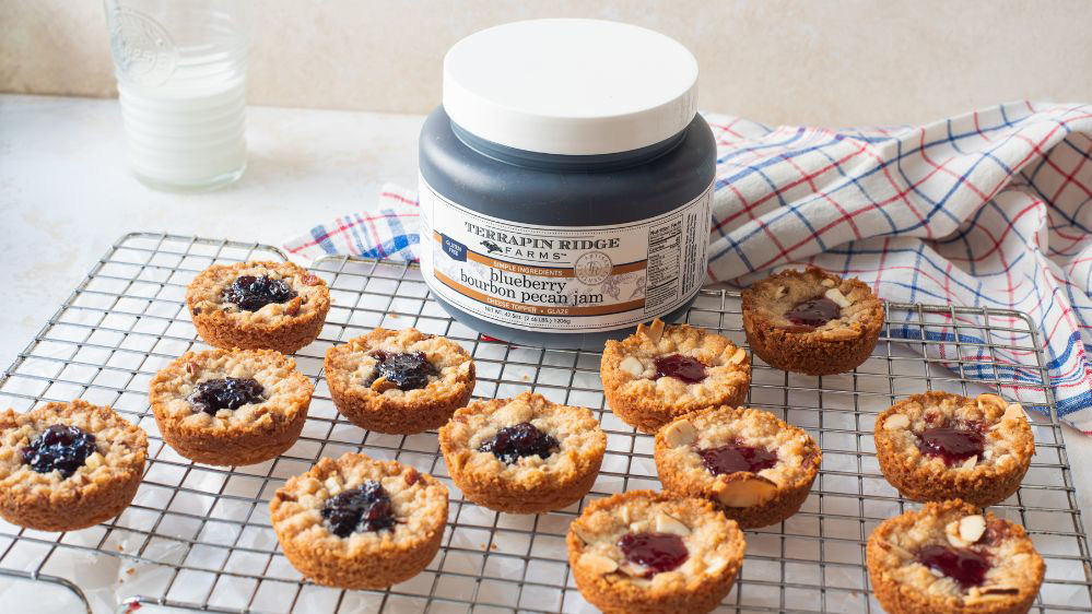 Image of Red, White & Blue Jammers (Cookies) Makes about 2 dozen cookies  Inspired by Dorie Greenspan's signature Jammers, these cookies have everything you want in a bite: a buttery, sablé-style crust, crumbly streusel, and a jammy center. We've simplified the traditionally fussy mold-and-cut method into a rustic press-in version made right in a standard muffin tin. We also add almond meal to the dough for extra nuttiness and a super tender texture. The real fun is in the two variations. We fill half with our Blueberry Bourbon Pecan Jam and top it with a pecan streusel, and the other half with our Sour Cherry Jam and an almond streusel that pairs nicely with cherries. They’re perfect for summer entertaining — think Fourth of July dessert table or a backyard BBQ. The dough and streusel can both be made ahead and the baked cookies store well at room temperature, so day-of is a breeze.