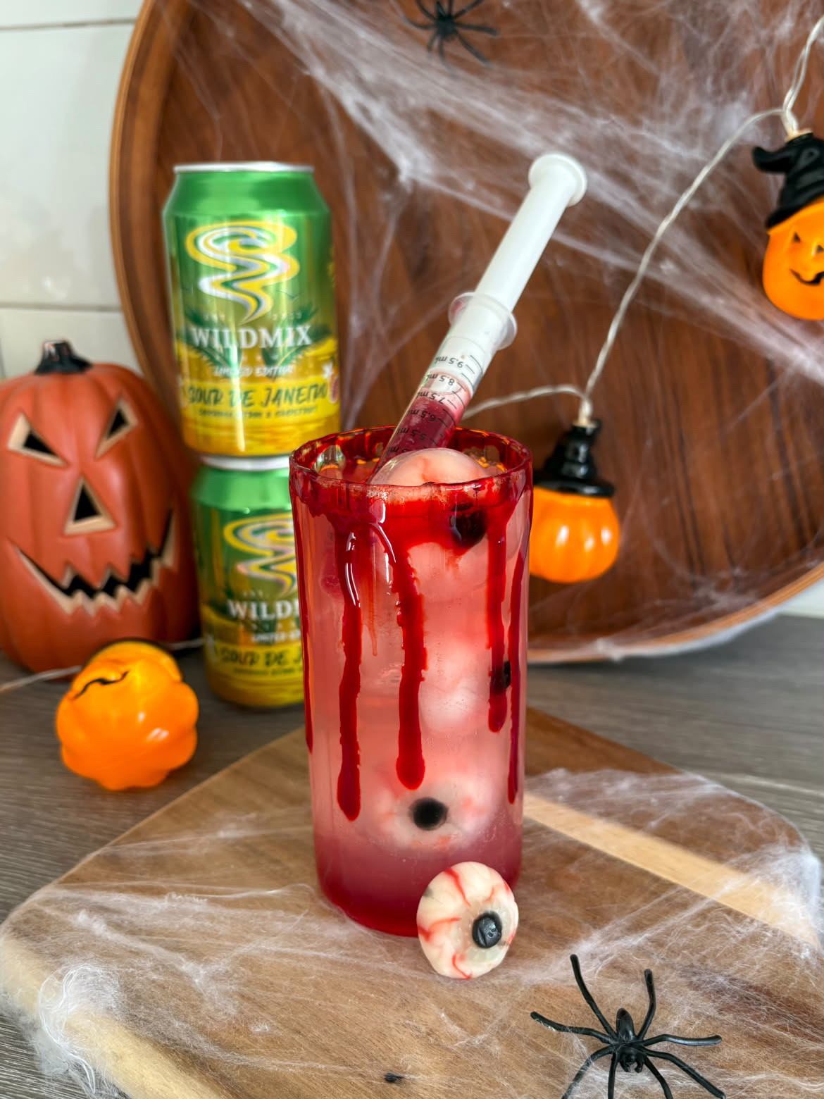 Alkoholfri halloweendrink med godisögon, röd glaskant och en spruta med grenadin