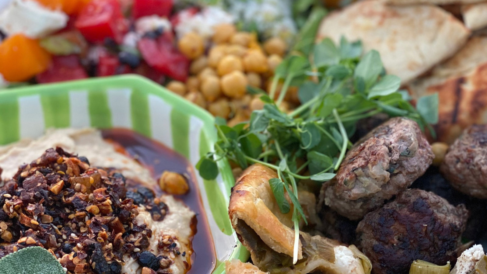 Mezze platter with grilled vegetables, lamb sliders, hummus, tomato and sheep cheese, fonio, yogurt dip and pita