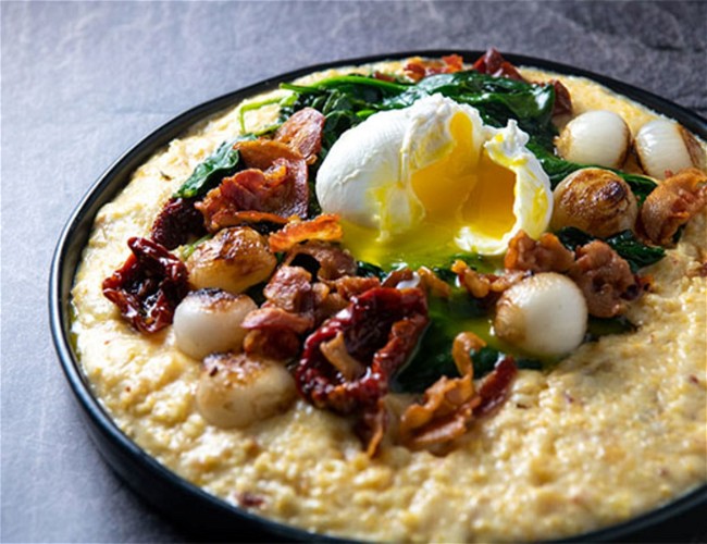 Image of Poached Eggs Over Polenta with Crispy Pancetta, Sun Dried Tomatoes, Wilted Spinach and Pearl Onions